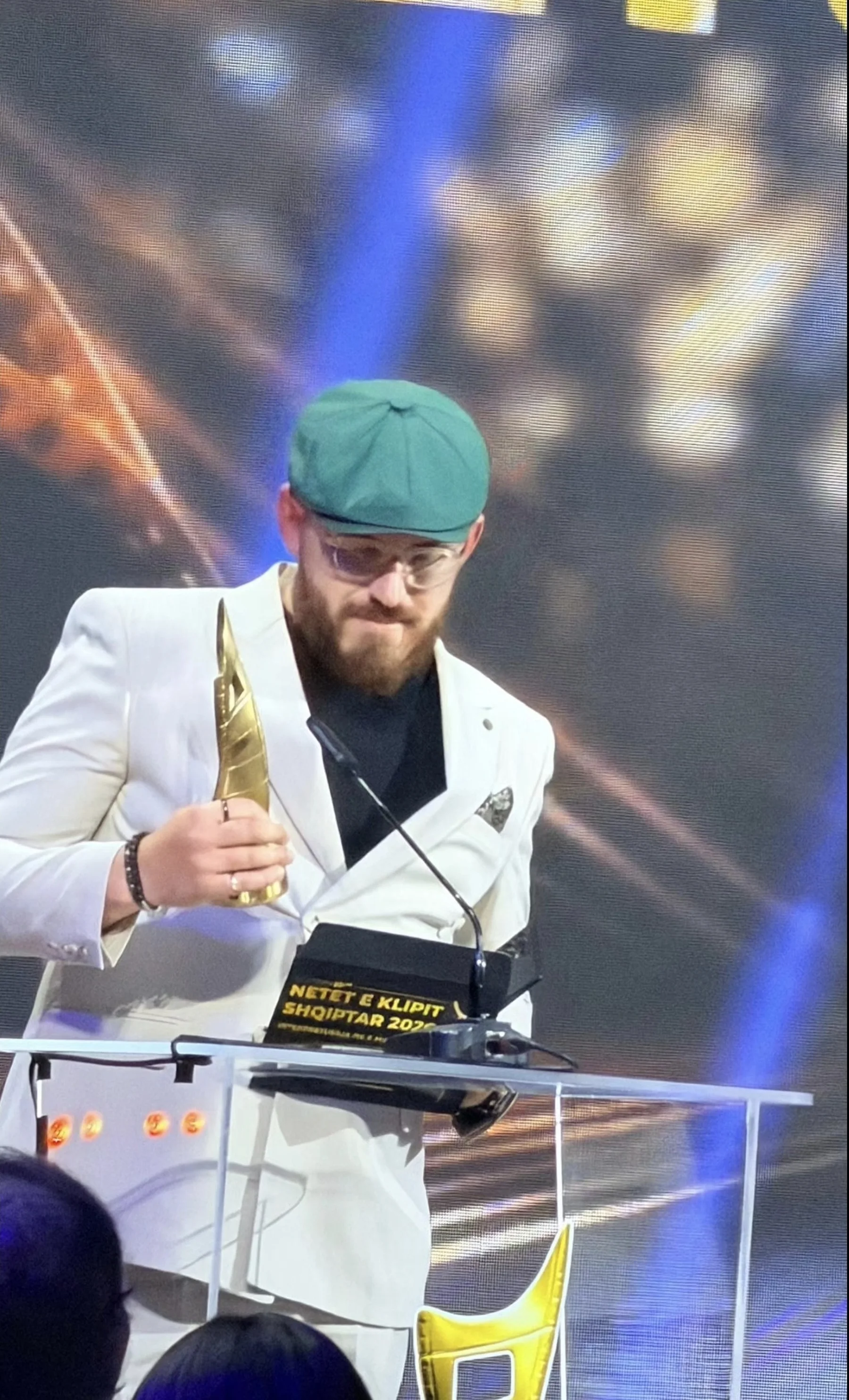 Ergys Shehu accepting an award at Netët e Klipit Shqiptar, wearing a green cap
