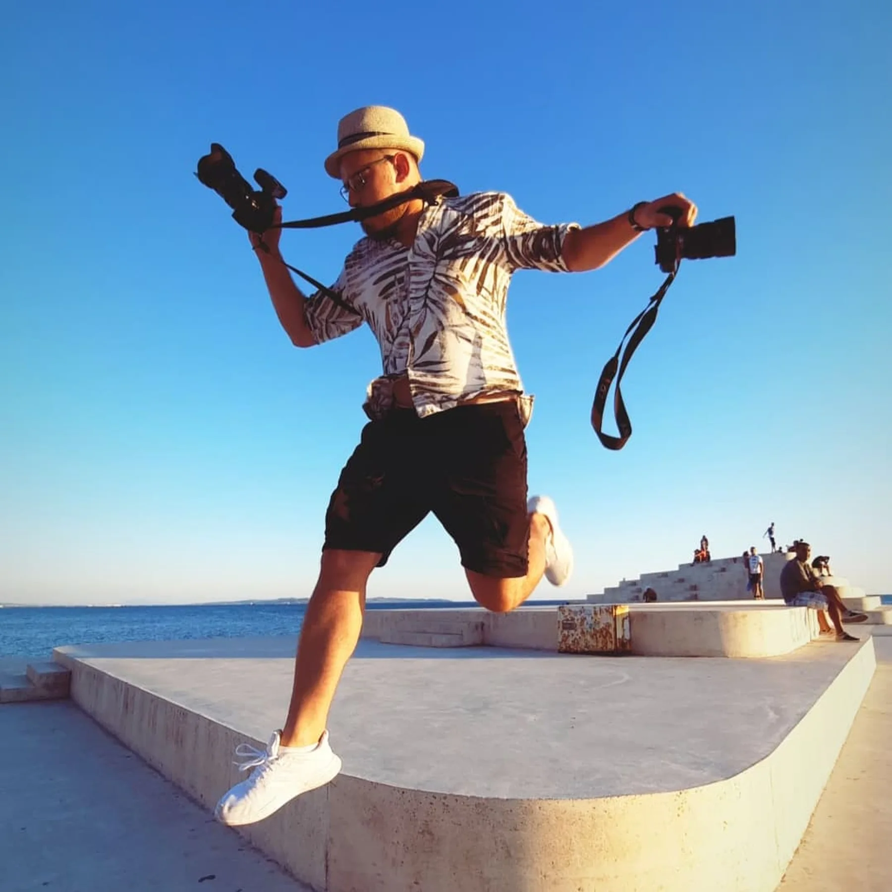 Ergys Shehu jumping with two cameras by the sea